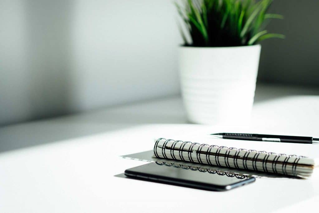Ein schwarzer Stift liegt auf einem Block neben einem Handy und einer Pflanze auf einem Schreibtisch