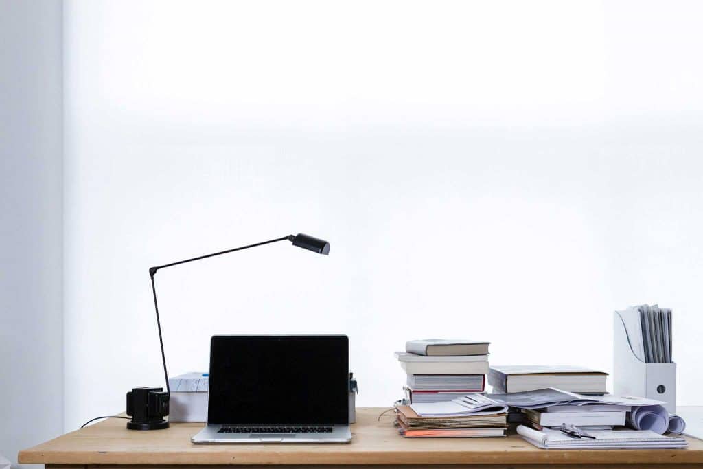 Schreibtisch mit MacBook, Tischlampe und Ordnern
